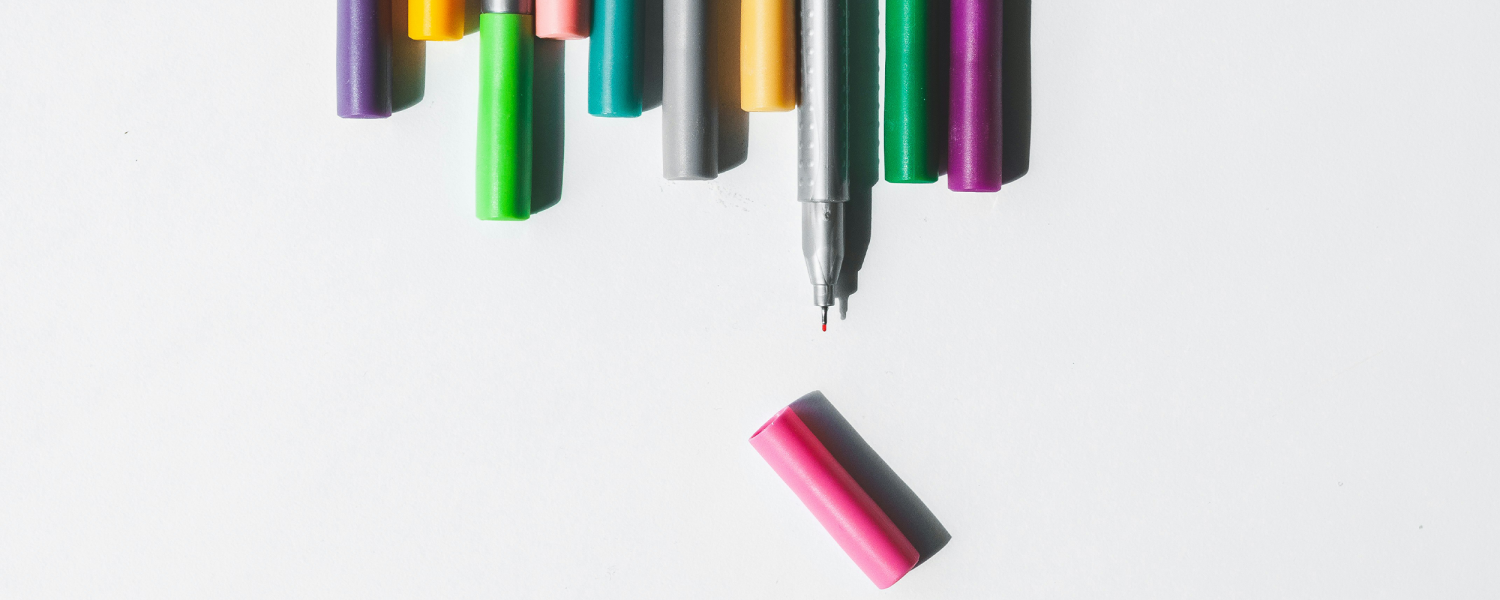 Coloured pens lined up, one pink pen with a lid taken off.